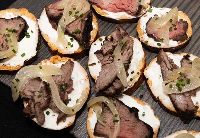 Perfect for catered events, these bread slices feature roast beef, cream, onions, and chives.