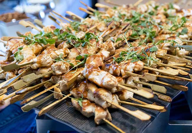 Minnesota Catering serves grilled chicken skewers topped with sauce and herbs, artfully arranged.
